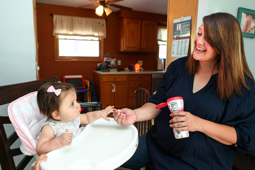 One year old Callie, who was conceived through in vitro fertilization, sits in a high chair reaching for a snack held out to her by her mother.