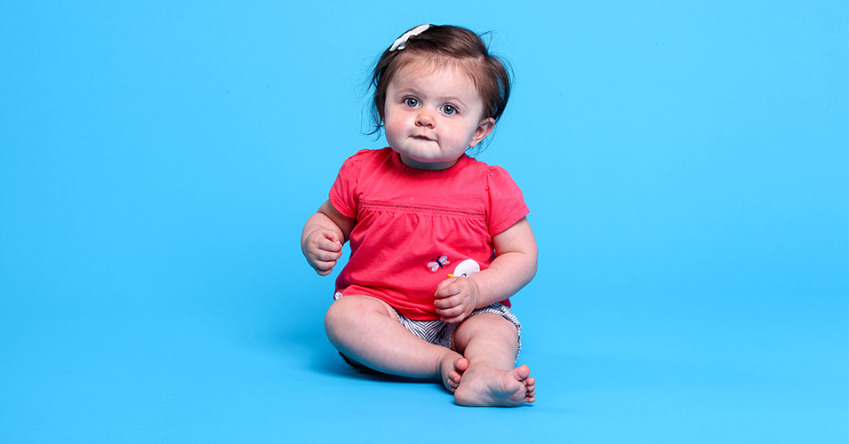 A baby poses in a bright pink onesie on an all blue background. Callie, who is almost 1, was born with the help of in vitro fertilization.