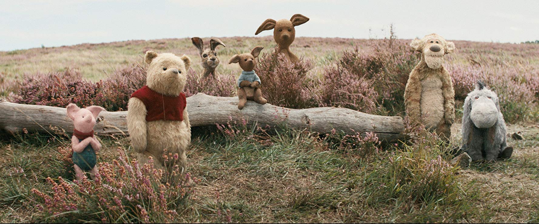 A scene from 'Christopher Robin," showing Piglet, Winnie the Pooh, Rabbit, Kanga, Roo, Tigger and Eeyore standing together in a field near a long old log.