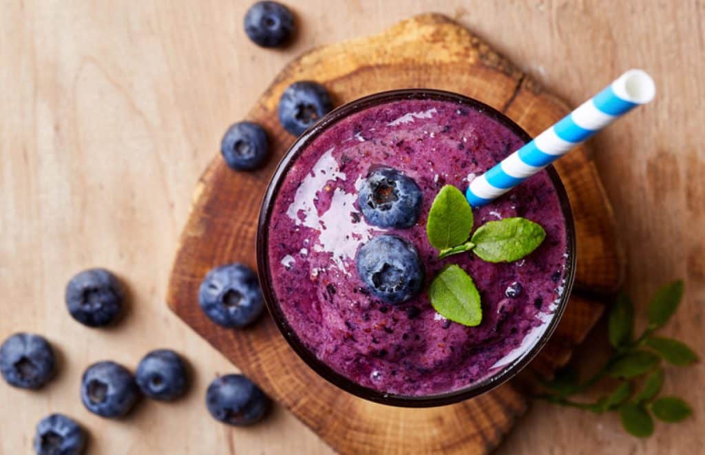 Glass of blueberry smoothie on wooden background from top view