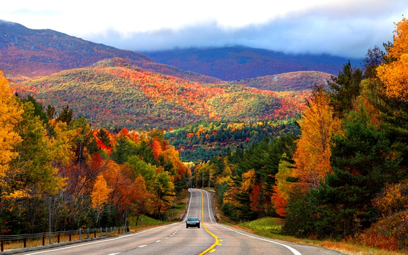 Car driving down highway with a view of the fall foliage and mountains