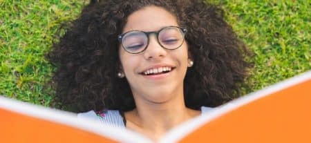 Young girl laying in the grass and reading book