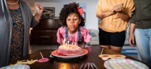 Black child blowing out birthday candles while family watches behind.