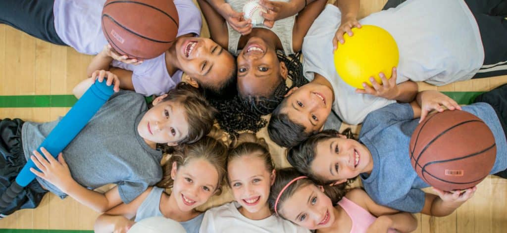 Group of kids laying on gym floor with sports balls