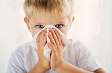 Young boy blowing nose into tissue.