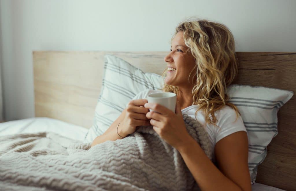 Happy mom enjoying in her coffee while spending morning time in bed.